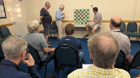 Players watching analysis arund demonstration chess board